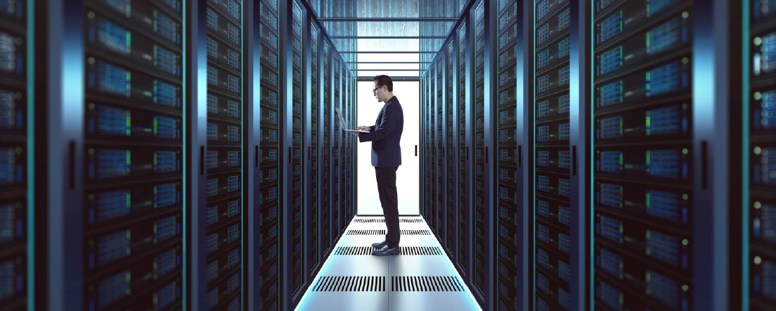 Man working on laptop inside a large server room